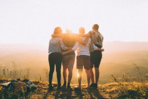 a group of 4 people facing the sun on a hill with arms linked behind