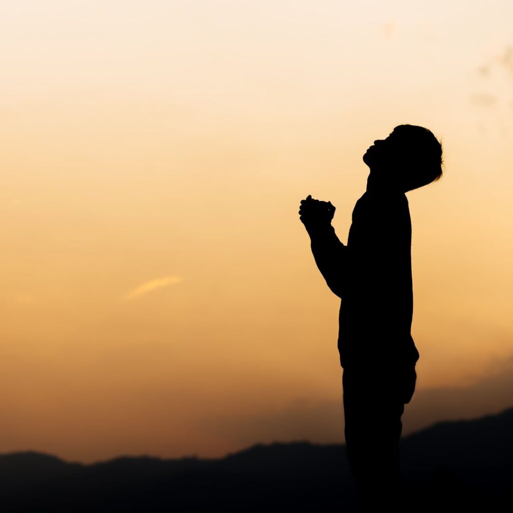 boy looking up to the sky praying with orange sunset in background